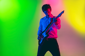 Image showing Young caucasian musician, guitarist playing on gradient background in neon light. Concept of music, hobby, festival