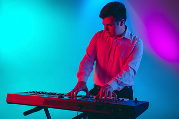 Image showing Young caucasian musician, keyboardist playing on gradient background in neon light. Concept of music, hobby, festival