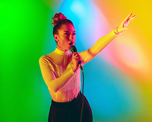 Image showing Young caucasian musician playing, singing on gradient background in neon light. Concept of music, hobby, festival