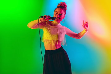 Image showing Young caucasian musician playing, singing on gradient background in neon light. Concept of music, hobby, festival