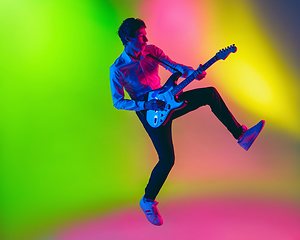 Image showing Young caucasian musician, guitarist playing on gradient background in neon light. Concept of music, hobby, festival