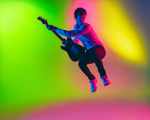 Image showing Young caucasian musician, guitarist playing on gradient background in neon light. Concept of music, hobby, festival