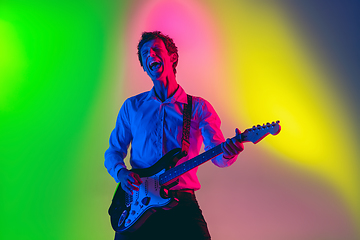 Image showing Young caucasian musician, guitarist playing on gradient background in neon light. Concept of music, hobby, festival