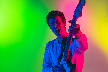 Image showing Young caucasian musician, guitarist playing on gradient background in neon light. Concept of music, hobby, festival