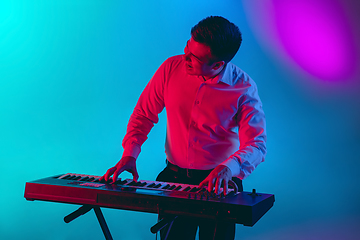 Image showing Young caucasian musician, keyboardist playing on gradient background in neon light. Concept of music, hobby, festival