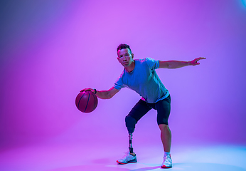 Image showing Athlete with disabilities or amputee isolated on gradient studio background. Professional male basketball player with leg prosthesis training and practicing in studio.