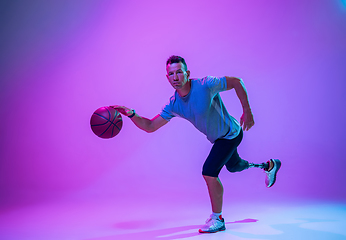 Image showing Athlete with disabilities or amputee isolated on gradient studio background. Professional male basketball player with leg prosthesis training and practicing in studio.