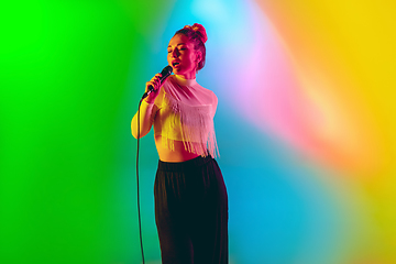 Image showing Young caucasian musician playing, singing on gradient background in neon light. Concept of music, hobby, festival