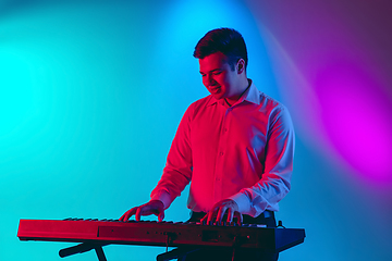 Image showing Young caucasian musician, keyboardist playing on gradient background in neon light. Concept of music, hobby, festival