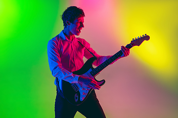 Image showing Young caucasian musician, guitarist playing on gradient background in neon light. Concept of music, hobby, festival