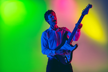 Image showing Young caucasian musician, guitarist playing on gradient background in neon light. Concept of music, hobby, festival