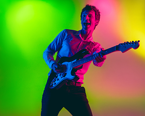 Image showing Young caucasian musician, guitarist playing on gradient background in neon light. Concept of music, hobby, festival