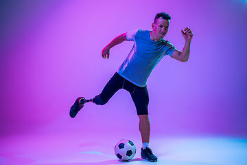 Image showing Athlete with disabilities or amputee isolated on gradient studio background. Professional male football player with leg prosthesis training and practicing in studio.