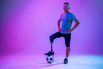Image showing Athlete with disabilities or amputee isolated on gradient studio background. Professional male football player with leg prosthesis training and practicing in studio.
