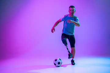 Image showing Athlete with disabilities or amputee isolated on gradient studio background. Professional male football player with leg prosthesis training and practicing in studio.