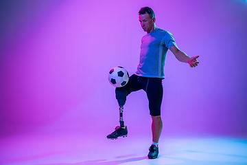 Image showing Athlete with disabilities or amputee isolated on gradient studio background. Professional male football player with leg prosthesis training and practicing in studio.