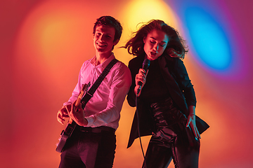 Image showing Young caucasian musicians, female singer and guitarist performing on gradient background in neon light. Concept of music, hobby, festival