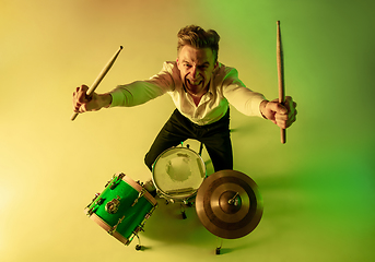 Image showing Young caucasian musician, drummer playing on gradient background in neon light. Concept of music, hobby, festival