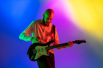 Image showing Young caucasian musician, guitarist playing on gradient background in neon light. Concept of music, hobby, festival