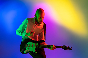 Image showing Young caucasian musician, guitarist playing on gradient background in neon light. Concept of music, hobby, festival