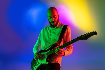 Image showing Young caucasian musician, guitarist playing on gradient background in neon light. Concept of music, hobby, festival