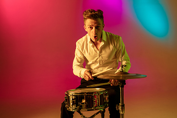 Image showing Young caucasian musician, drummer playing on gradient background in neon light. Concept of music, hobby, festival
