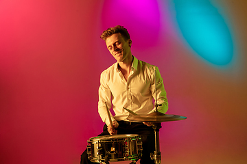 Image showing Young caucasian musician, drummer playing on gradient background in neon light. Concept of music, hobby, festival