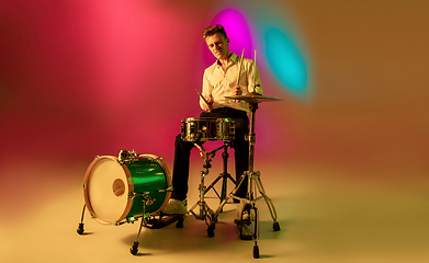 Image showing Young caucasian musician, drummer playing on gradient background in neon light. Concept of music, hobby, festival