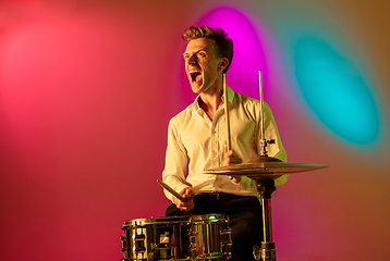 Image showing Young caucasian musician, drummer playing on gradient background in neon light. Concept of music, hobby, festival