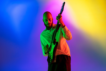 Image showing Young caucasian musician, guitarist playing on gradient background in neon light. Concept of music, hobby, festival