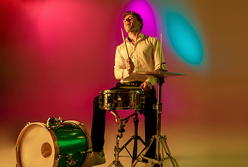 Image showing Young caucasian musician, drummer playing on gradient background in neon light. Concept of music, hobby, festival