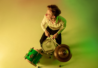 Image showing Young caucasian musician, drummer playing on gradient background in neon light. Concept of music, hobby, festival