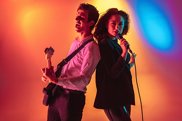 Image showing Young caucasian musicians, female singer and guitarist performing on gradient background in neon light. Concept of music, hobby, festival