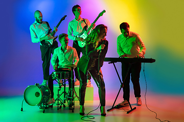 Image showing Young caucasian musicians, band playing on gradient background in neon light. Concept of music, hobby, festival