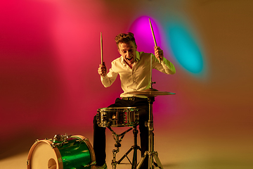 Image showing Young caucasian musician, drummer playing on gradient background in neon light. Concept of music, hobby, festival