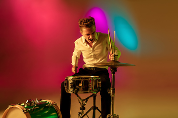 Image showing Young caucasian musician, drummer playing on gradient background in neon light. Concept of music, hobby, festival