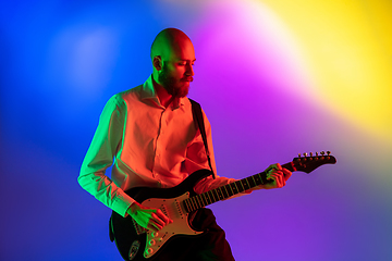 Image showing Young caucasian musician, guitarist playing on gradient background in neon light. Concept of music, hobby, festival