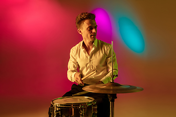 Image showing Young caucasian musician, drummer playing on gradient background in neon light. Concept of music, hobby, festival