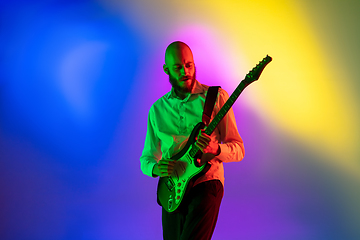 Image showing Young caucasian musician, guitarist playing on gradient background in neon light. Concept of music, hobby, festival