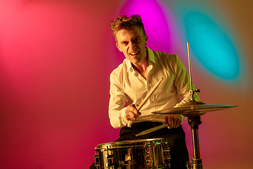 Image showing Young caucasian musician, drummer playing on gradient background in neon light. Concept of music, hobby, festival