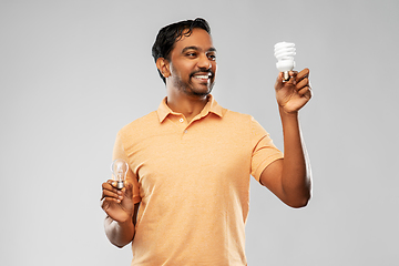 Image showing smiling indian man comparing different light bulbs