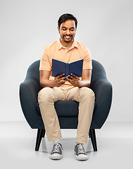 Image showing happy young indian man reading book in chair