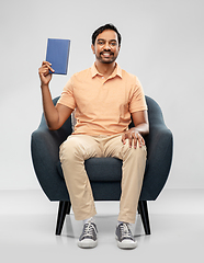 Image showing happy young indian man showing book in chair