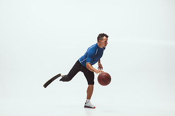 Image showing Athlete with disabilities or amputee isolated on white studio background. Professional male basketball player with leg prosthesis training and practicing in studio.