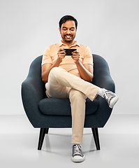 Image showing happy young indian man with smartphone in chair