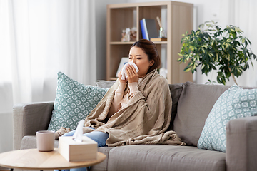 Image showing sick asian woman blowing nose with tissue at home