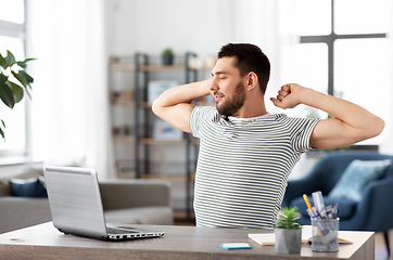 Image showing happy man with laptop stretching at home office