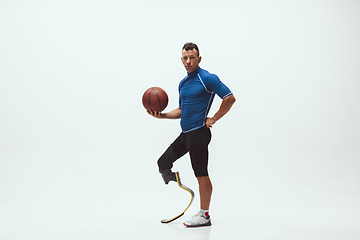 Image showing Athlete with disabilities or amputee isolated on white studio background. Professional male basketball player with leg prosthesis training and practicing in studio.