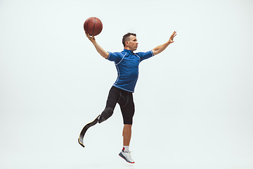 Image showing Athlete with disabilities or amputee isolated on white studio background. Professional male basketball player with leg prosthesis training and practicing in studio.