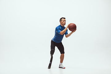 Image showing Athlete with disabilities or amputee isolated on white studio background. Professional male basketball player with leg prosthesis training and practicing in studio.
